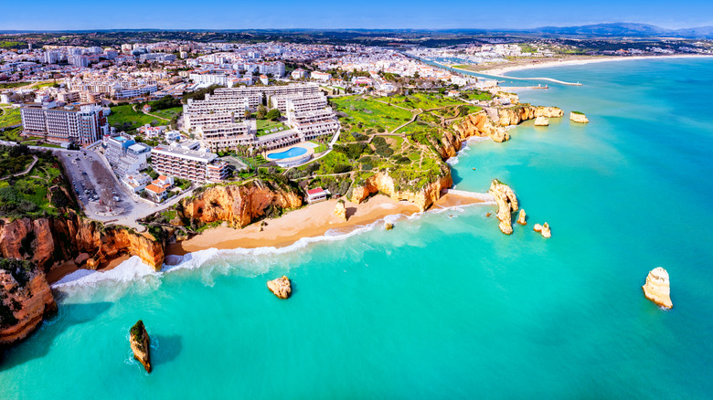 A beach with turquoise water sits below the city of Lagos in Portugal