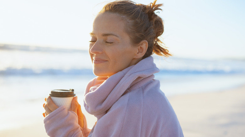 A woman enjoys a coffee by the beach