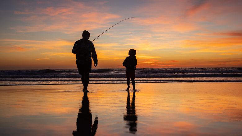 A family of two fishing together on a beach at sunset