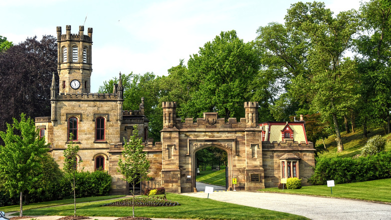 Gatehouse of Allegheny Cemetery, a majestic brown stone building with towers surrounded by green trees under a cloudy sky