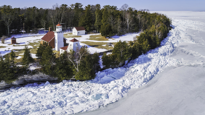 An aerial photo of a white Door County Lighthouse next to icy Lake Michigan