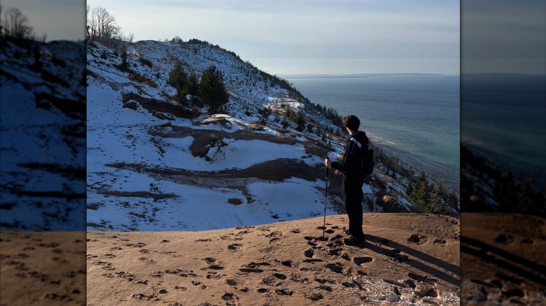 A hiker on top of the sandy dunes at Sleeping Bear with Lake Michigan and snow-covered dunes in the background