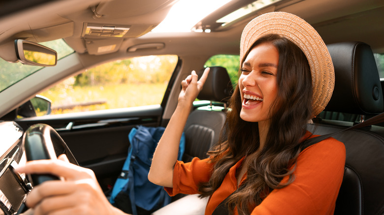 A woman in a wide-brimmed hat driving in a car on a sunny day while smiling