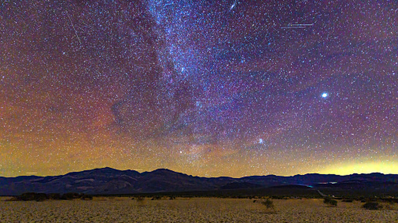 The Milky Way glows over cracked earth and dry mountains in Death Valley National Park.