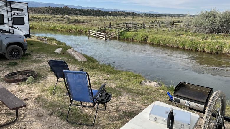 An RV and camping chairs overlooking a river at the Riverside Ranch RV Park, Motel, & Campground