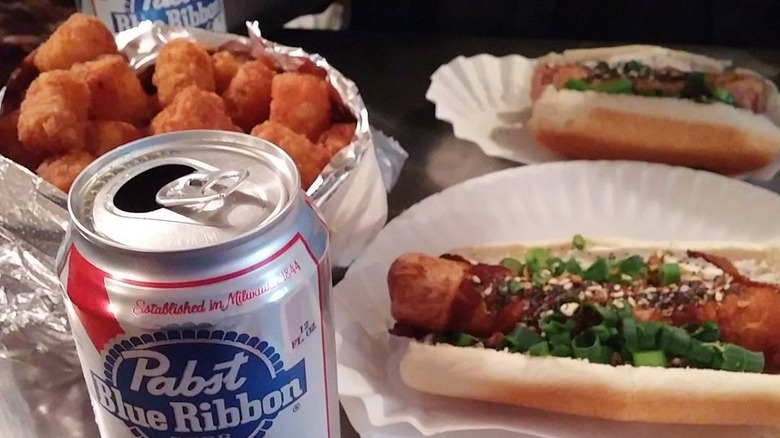 a tablescape showing hot dogs, tater tots, and PBRs