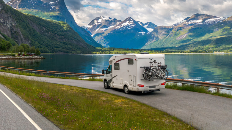 A motorhome driving by a lake in the mountains