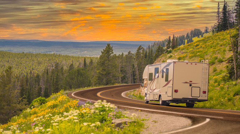 An RV driving through a hilly, forested landscapes at sunset