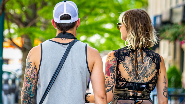 A tatted-up couple strolls down a tree-lined street in summertime in Asheville, North Carolina