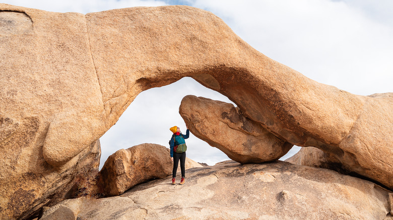 A woman stands under the famous Arch Rock in Joshua Tree National Park