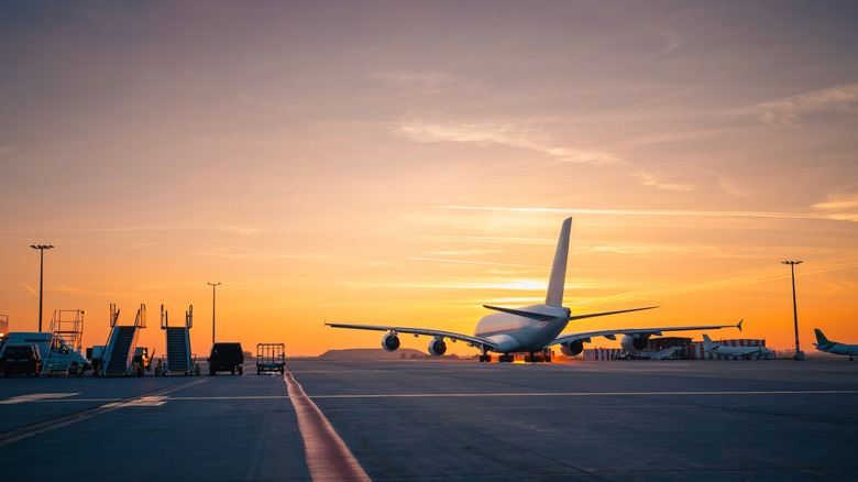 Wide shot of airplane about to take off from tarmac as sun sets