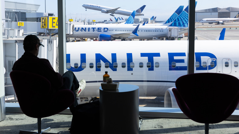 A silhouetted man sitting in an airport in the United Airlines terminal watches United planes on the tarmac