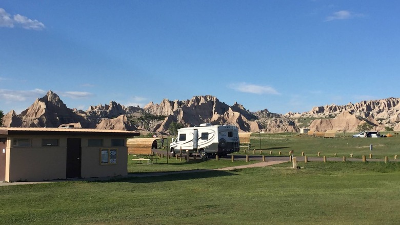 A restroom and RV in the foreground of a campsite backed by geological formations in the distance