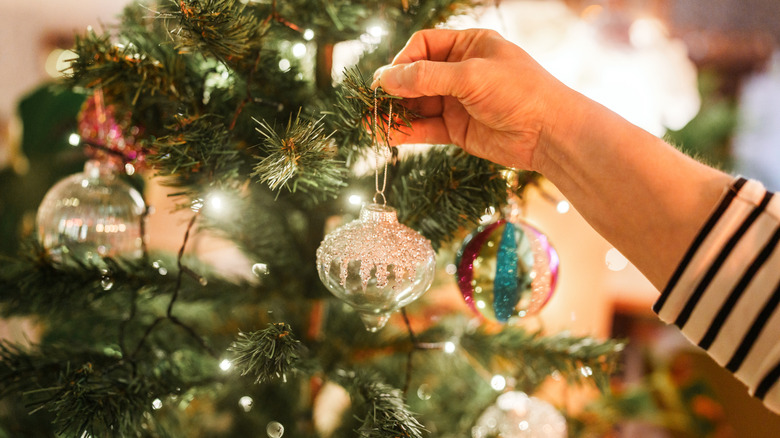 Hand placing an ornament on a Christmas tree