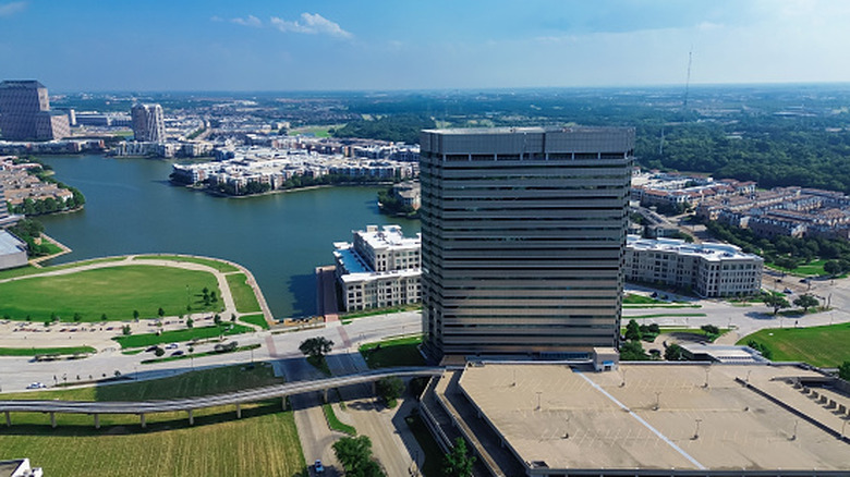Office building rises above other high rise developments, motorway, and lake in Irving, Texas