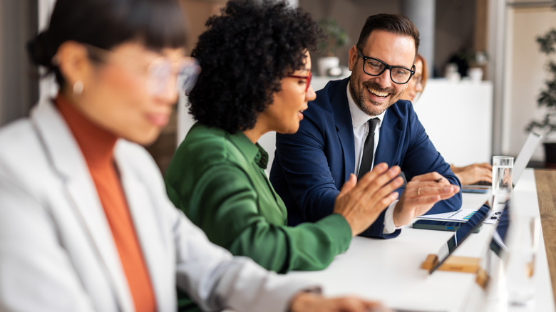 Bespectacled workers happily confer over laptops in an office setting