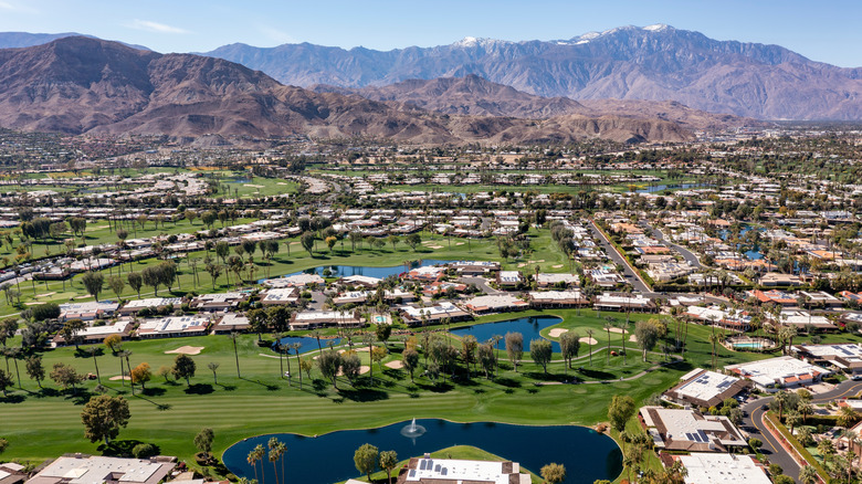 Aerial view of houses and golf courses in Palm Springs backed by mountain ranges.