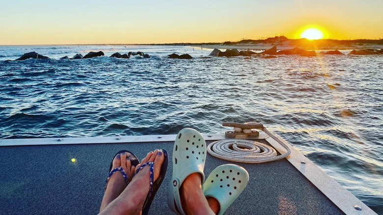 The feet of two passengers on the Carolina Runner overlooking water and the sunset.