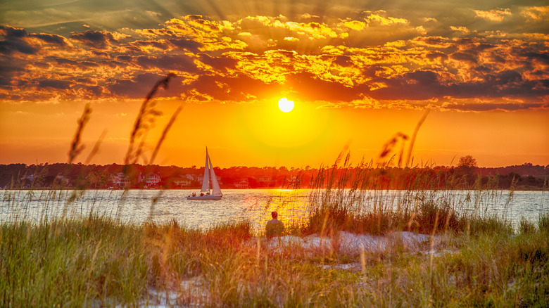 A sailing boat cruising past a sandy shoreline in Wrightsville Beach.
