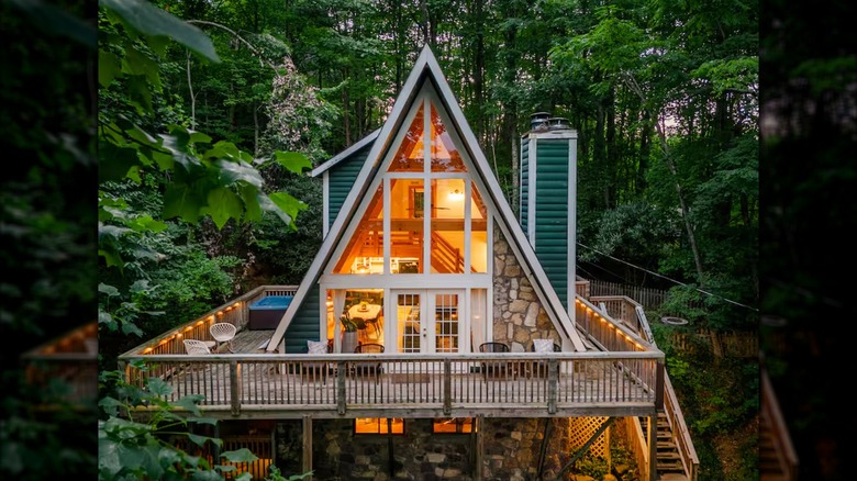 A green A-frame home surrounded by green trees