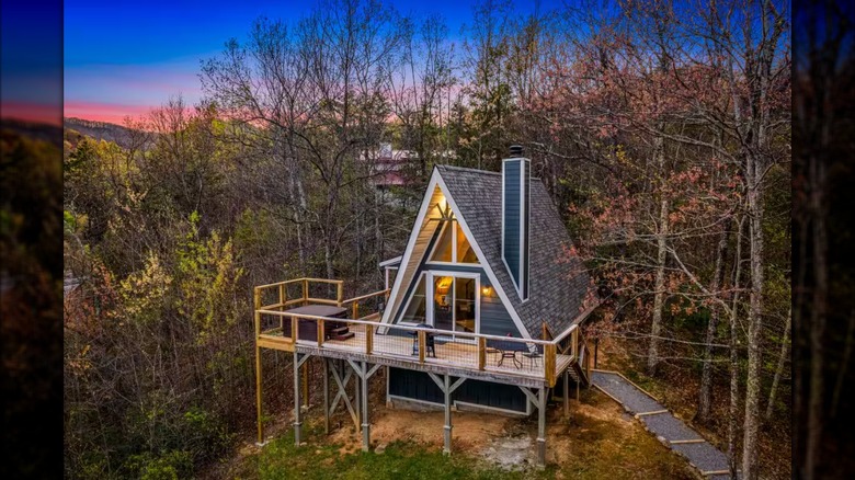 An A-frame home surrounded by woods with a sunrise