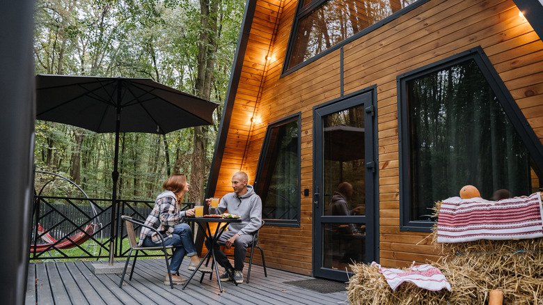 A couple sitting outside by an A-frame cabin
