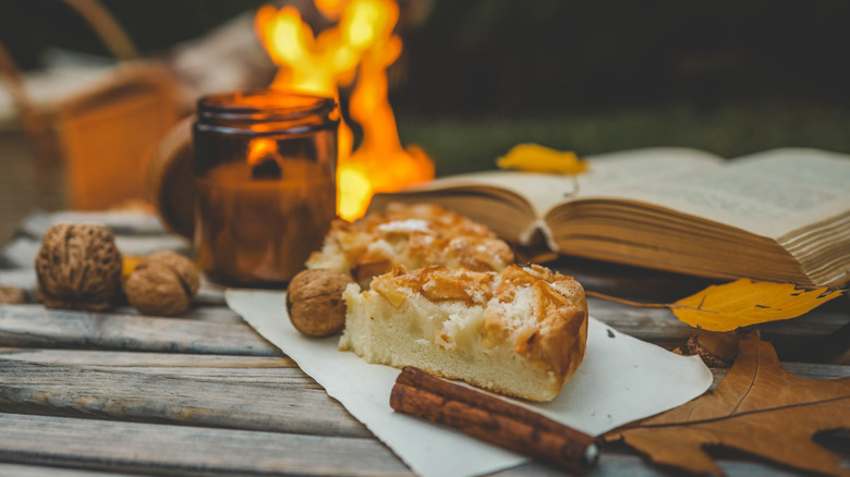 Apple pie next to a candle, fireplace, cinnamon stick, and book