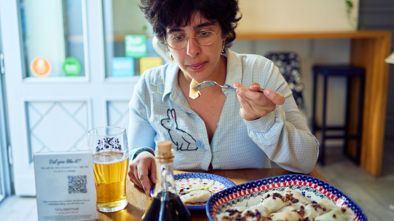 A woman eats pierogies with a beer inside a cute cafe