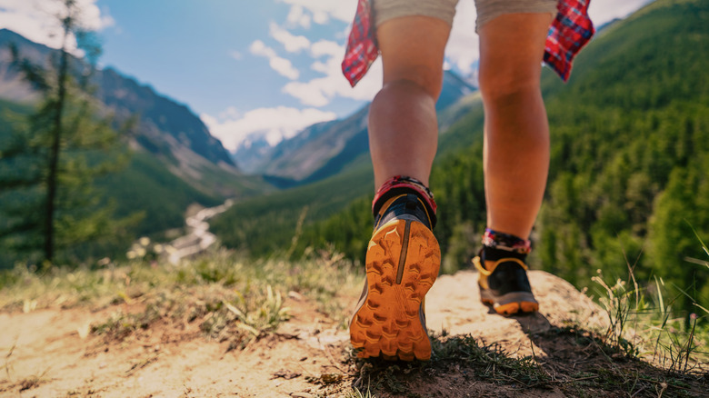 Woman's feet hiking in trail runners in front of a scenic valley
