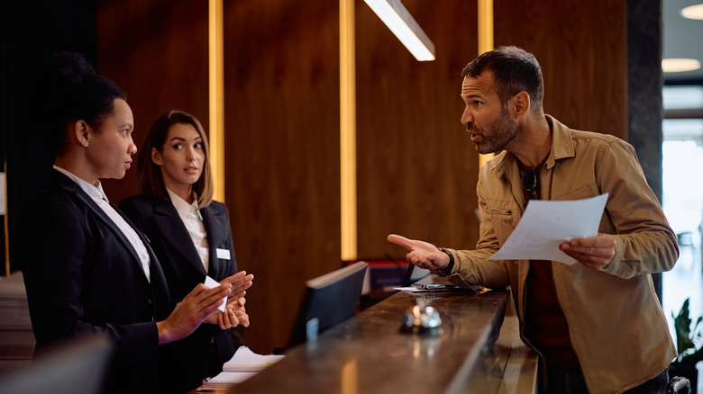 Angry man talking with receptionists about hotel bill