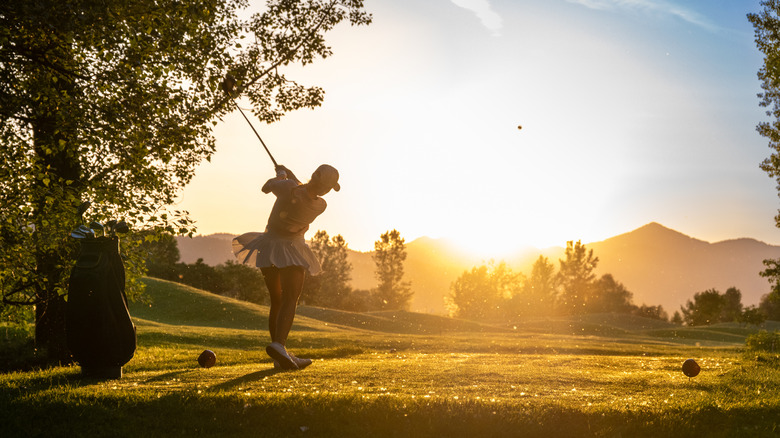 Golfer in mid-swing at sunset on course