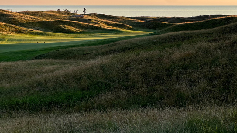 Rolling hills and a green fairway with Lake Michigan and a sunset in the background