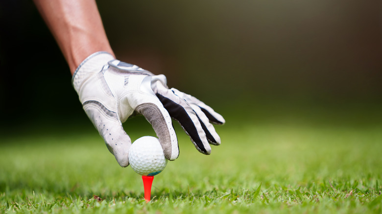 Golfer placing ball on tee with gloved hand