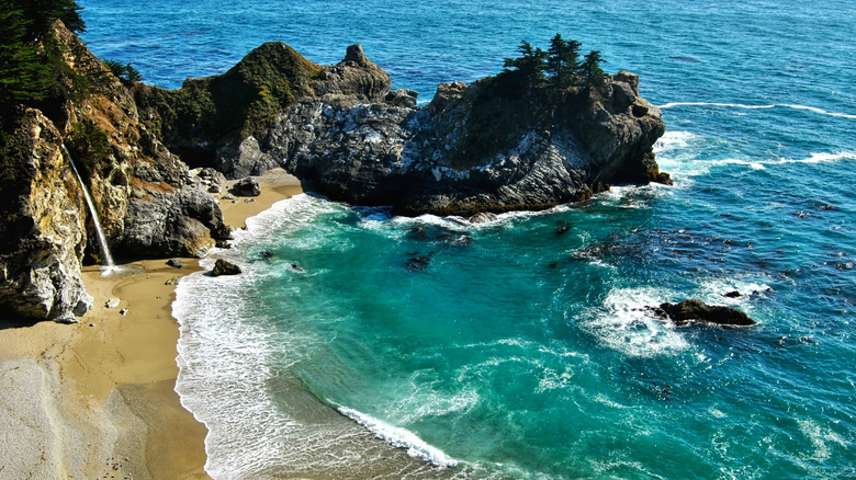 A waterfall spills onto an empty beach cove at a state park in Big Sur.