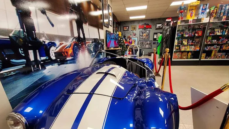 Blue car with white stripes in the foreground, with display cases of comic book memorabilia in the background
