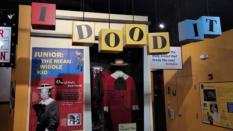 Display in the Red Skelton museum, with sign reading "I Dood It" and the red costume for Junior, with orange walls in the background