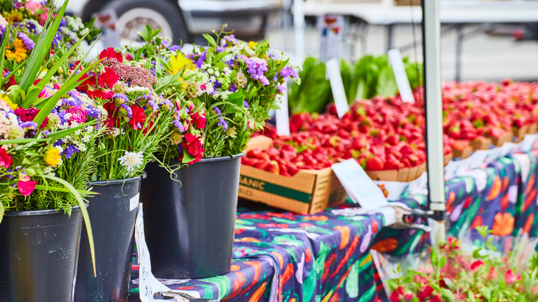 A table displays mixed flower bouquets and ripe strawberries at a Sacramento farmers' market.