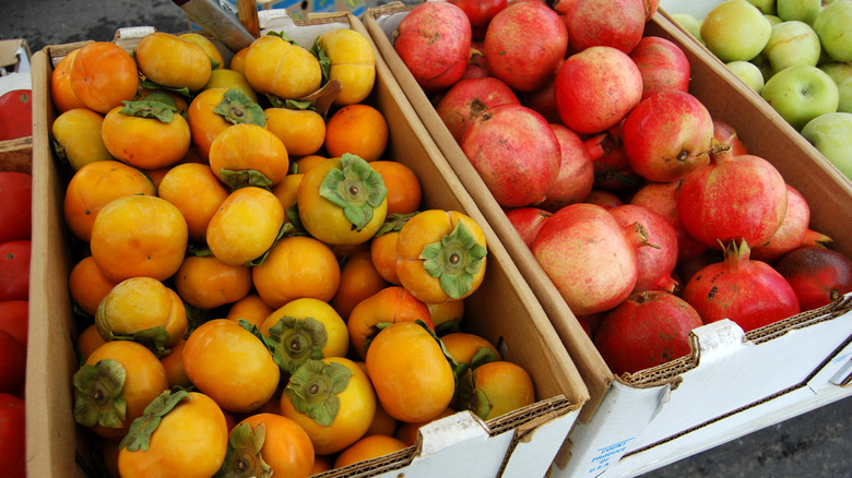 White cardboard boxes filled with persimmons and pomegranate at a farmers' market in Sacramento.
