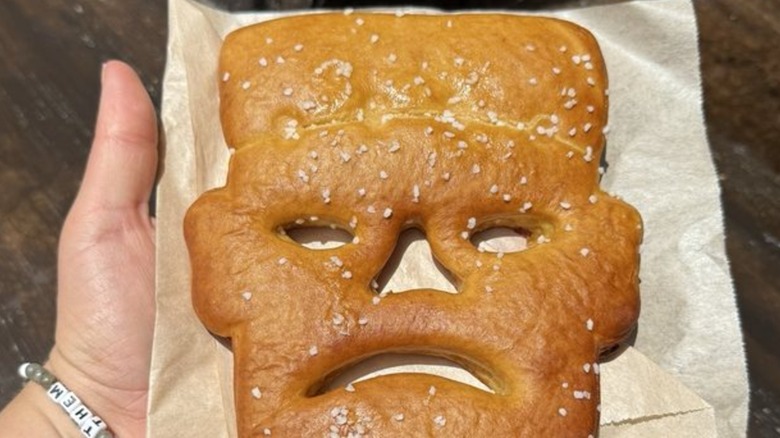 A hand holds out a pretzel with a Frankenstein-shaped head