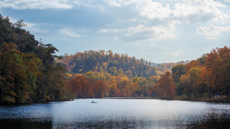 a lone kayak cuts through the calm surface of Broken Bow Lake, Oklahoma, surrounded by fall foliage