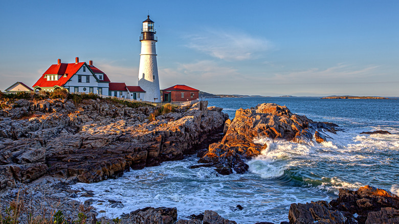 A landscape of the Maine coast shows rocky shores and a whitewashed lighthouse