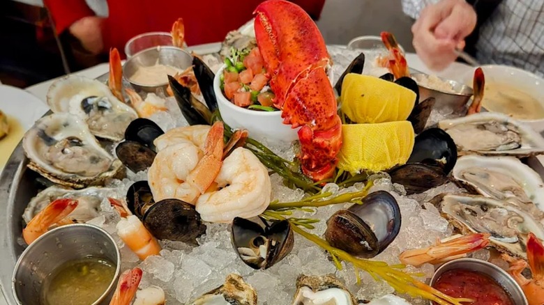 A bowl of seafood on ice with sauces and lemon on a restaurant table