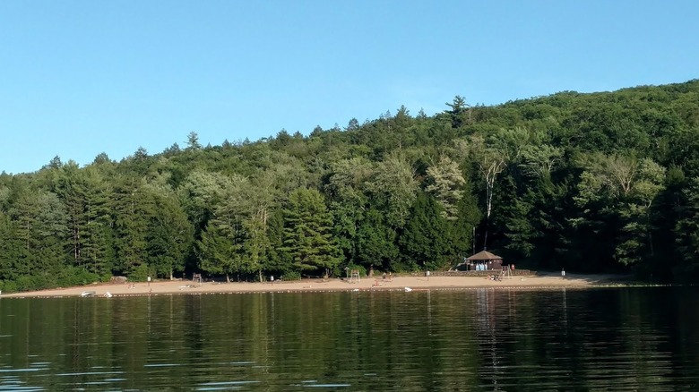 Laurel Lake's calm waters and sandy beach shore; a small building sits towards the back of the beach, surrounded by dense forest