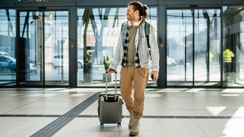 A person traveling through an airport, wheeling a carry-on suitcase behind them