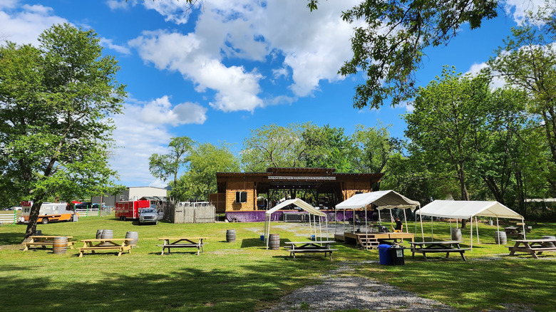 Grassy area with picnic tables, white canopies, and a wooden covered stage