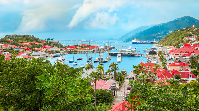 Panoramic landscape view of the port of Gustavia in Saint Barthélemy with boats, yachts and luxury ships. Houses with red roofs along the bay connecting to the Caribbean Sea