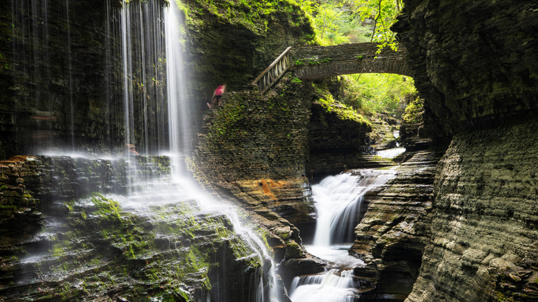A narrow rocky canyon with a bridge spanning across and two waterfalls