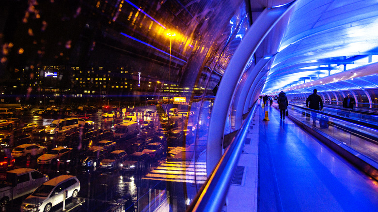 A covered travelator and walkway at Manchester airport lit up at night with colored mood lighting