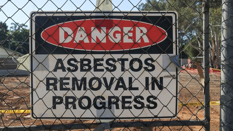 Black, white and red "Danger Asbestos Removal In Progress" warning site on wire fence