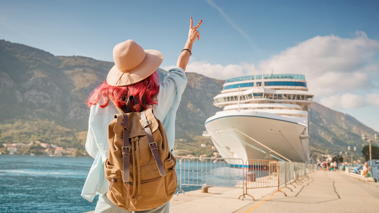 Tourist wearing backpack and hat gesturing near cruise ship at Kotor bay, Montenegro
